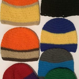 Peut inclure: Une collection de sept bonnets crochetés avec divers motifs en blocs de couleurs, incluant orange, jaune, beige, blanc, gris, noir, bleu, rouge, violet et vert. Le texte "Color- block Beanie 2 Colors" est visible en haut de l'image.