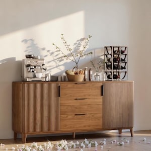 May include: A light brown wooden sideboard with a coffee machine, wine rack, and decorative items. The sideboard has three drawers and two doors with vertical grooved detailing. A small espresso machine sits on the left side.