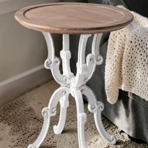 May include: A small, round side table with a light brown tabletop and ornate white legs. The tabletop has a raised edge. The legs are curved and feature decorative scrollwork. The table is approximately 24 inches in height.