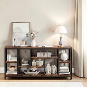 May include: A dark brown and black console table with multiple shelves, displaying decorative items like books, vases, and lanterns. A lamp with a white shade sits on the table. The table is made of wood and metal.