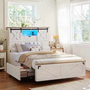 May include: A white bed frame with a headboard featuring a barn door design and a built-in shelf with blue lighting. The bed has a pull-out drawer and is adorned with pillows and a patterned comforter. The headboard is accented with a wooden top.