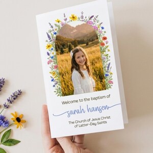 May include: A white baptism program card featuring a central arched photo of a child in a field. The arch is framed by colorful watercolor wildflowers. Text reads: Welcome to the baptism of sarah hansen, The Church of Jesus Christ of Latter-Day Saints.