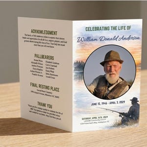 May include: A folded memorial card with text and a portrait of a man in a hat. The card reads "Celebrating the Life of William Donald Anderson" and includes dates and locations. The card is on a wooden surface.