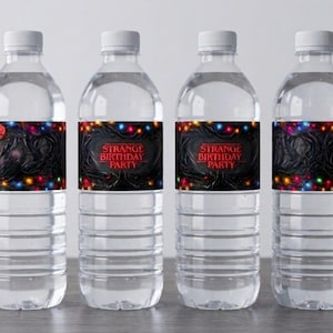 May include: Four clear plastic water bottles with white lids. Each bottle features a label with the text "STRANGE BIRTHDAY PARTY" in red on a black background, a string of lights, and a dark, textured design.