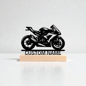 Puede incluir: Silueta negra de motocicleta deportiva con detalles blancos, montada sobre una base de madera. La base tiene el texto "CUSTOM NAME". La moto es una representación detallada.