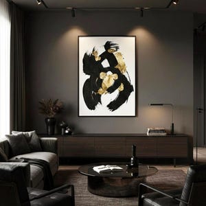 May include: A rectangular wall art piece featuring bold, sweeping black brushstrokes and metallic gold leaf accents on a white background, enclosed in a thin black frame, displayed prominently on a dark gray wall above a long wooden media console.