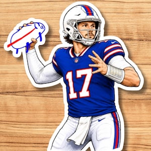 May include: A die-cut sticker featuring a football player in a blue jersey with the number 17 in white and red, wearing a white helmet and white pants. The player is throwing a hand-drawn, blue and red doodle of a football with a smiling face.