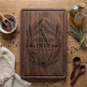 Może przedstawiać: Prostokątna drewniana deska do krojenia z wygrawerowanymi w środku słowami "POTION PREP" i "chop, crush, brew". Deska otoczona jest botanicznym wzorem. Inne elementy to miska z przyprawami, olej, zioła i drewniane łyżki.