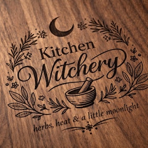 May include: A wooden cutting board with the words "Kitchen Witchery" and the phrase "herbs, heat & a little moonlight" engraved in a decorative font. The design includes a crescent moon, floral elements, and a mortar and pestle.