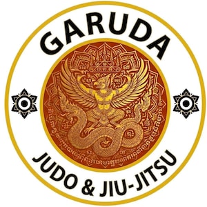 Pode incluir: Emblema circular com a palavra "GARUDA" em preto, arqueada na parte superior. O centro apresenta uma ilustração dourada de uma criatura mítica. As palavras "JUDO & JIU-JITSU" estão na parte inferior. O emblema é contornado por um anel dourado.