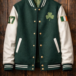 Könnte beinhalten: Grün-weiße Collegejacke mit goldenen Knöpfen, einem Kleeblatt-Patch und der Zahl 17 auf dem linken Ärmel. Der rechte Ärmel zeigt eine irische Flagge. Die Jacke hat weiße Streifen an Kragen, Bündchen und Saum.
