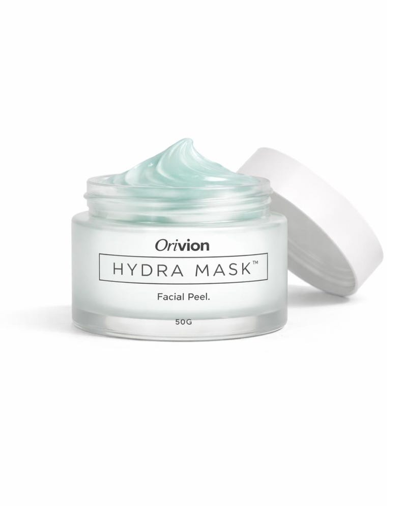 May include: A clear glass jar of "Hydra Mask" facial peel by Orivion. The jar contains a light blue gel, with the lid resting beside it. The jar is labeled "50G".