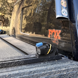 May include: Black truck bed cover with a black camera mounted on it. A cylindrical container with cat faces is attached to the side of the truck. The FOX logo is visible on the truck.
