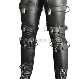 Puede incluir: Pantalones de cuero negro con múltiples correas, hebillas y cremalleras. El diseño ajustado incluye una cintura alta y se extiende hasta los tobillos. El texto "theleatherdungeon" es visible en la pierna izquierda.