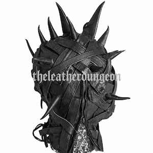 Puede incluir: Máscara de cuero negro con diseño de púas. La máscara presenta un patrón de cuero tejido y un cierre de cremallera. El texto "theleatherdungeon" es visible en el lateral. La máscara tiene múltiples púas afiladas.