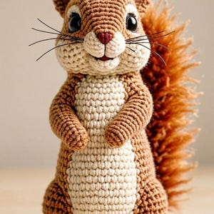 Op de afbeelding: Een handgemaakt gehaakt eekhoornspeeltje in bruin- en crèmetinten. De eekhoorn heeft een pluizige staart, zwarte ogen en snorharen. Het speelgoed staat rechtop, met de pootjes tegen elkaar, wat het gedetailleerde haakwerk laat zien.