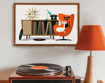 May include: A framed mid-century modern art print featuring a retro living room scene with a record player, orange lamp, and a stylized illustration of a record cabinet, clock, and two cats in an orange chair. The turntable is brown.