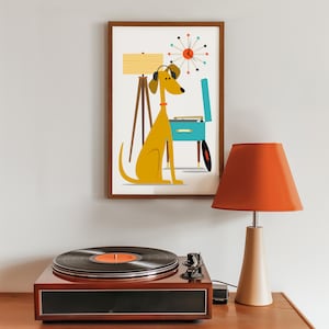 May include: A framed print featuring a yellow dog wearing headphones, listening to a record player. The print also includes a mid-century modern clock and a lamp. A record player with a black vinyl record is on a wooden surface, next to a lamp with an orange shade.