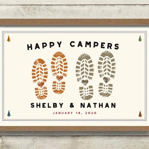 Pode incluir: Impress&atilde;o emoldurada com as palavras "HAPPY CAMPERS" em preto acima de dois pares de pegadas de botas com detalhes de cora&ccedil;&atilde;o. Os nomes "Shelby & Nathan" e a data "January 18, 2020" est&atilde;o abaixo. A moldura &eacute; marrom.