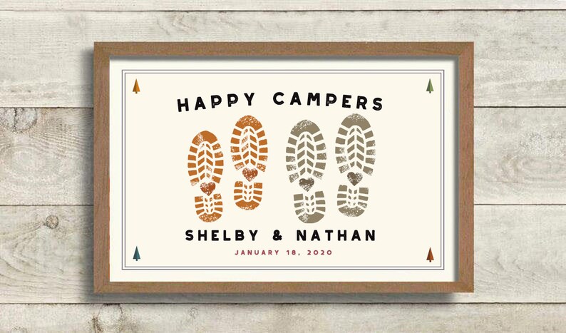Pode incluir: Impress&atilde;o emoldurada com as palavras "HAPPY CAMPERS" em preto acima de dois pares de pegadas de botas com detalhes de cora&ccedil;&atilde;o. Os nomes "Shelby & Nathan" e a data "January 18, 2020" est&atilde;o abaixo. A moldura &eacute; marrom.