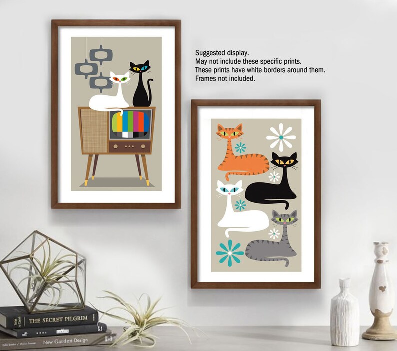 May include: Two framed prints featuring retro-style illustrations of cats. The first print shows three cats in front of a vintage television set. The second print shows four cats with a floral design.