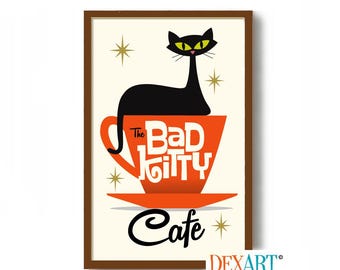 May include: A framed print featuring a black cat with yellow eyes perched atop an orange coffee cup. The cup reads "The Bad Kitty Cafe" in white lettering, with the word "Cafe" in black script below. Gold starbursts accent the off-white background.