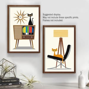 May include: Two framed prints with a retro mid-century modern theme. The first print features a black cat sitting on top of a vintage television with a clock behind it. The second print features an orange cat sitting in a black chair with a tripod lamp behind it.  "Suggested display. May not include these specific prints. Frames not included."