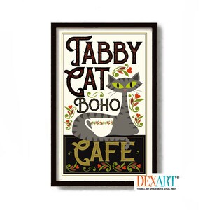 May include: A vintage-style sign with the text "Tabby Cat Boho Cafe" in a stylized font. A gray cat with green eyes is sitting on a table with a cup of coffee. The sign has a black frame and a white background with red, green, and black accents.