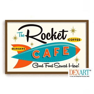 May include: A framed vintage-style sign for "The Rocket Cafe" with a teal rocket ship design. The sign includes the words "BURGERS" and "COFFEE", and the phrase "Good Food Served Here!" in a retro font.