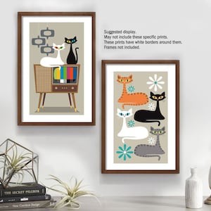 May include: Two framed prints featuring retro-style illustrations of cats. The first print shows three cats in front of a vintage television set. The second print shows four cats with a floral background. Both prints have a beige background.