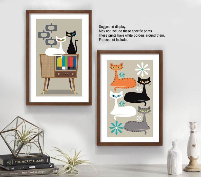 May include: Two framed prints featuring retro-style illustrations of cats. The first print shows three cats in front of a vintage television set. The second print shows four cats with a floral background. Both prints have a beige background.