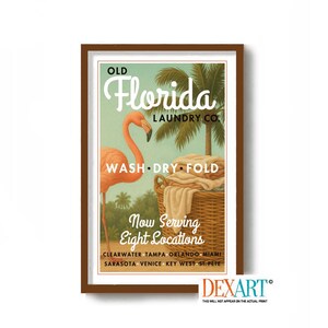 May include: A framed vintage-style print featuring a flamingo and palm trees. The text reads "Old Florida Laundry Co. WASH DRY FOLD" with "Now Serving Eight Locations" below. The print has a brown frame and a retro aesthetic.