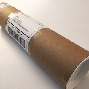 Puede incluir: Un tubo de cart&oacute;n marr&oacute;n con una tapa blanca. Una etiqueta blanca con el texto "USPS TRACKING # - EP" est&aacute; pegada al tubo.