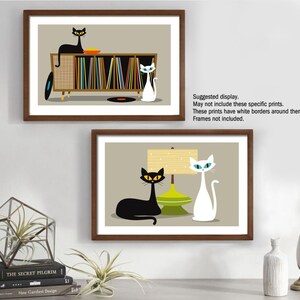 May include: Two framed illustrations of cats in a mid-century modern style. The top image shows a black cat sitting on a record player with a white cat standing next to it. The bottom image shows a black cat lying down next to a white cat and a lamp with a green shade.