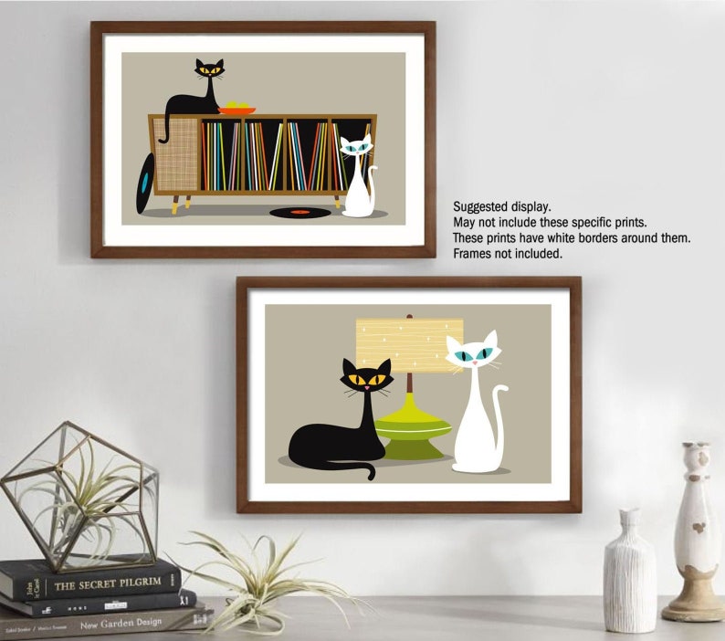 May include: Two framed illustrations of cats in a mid-century modern style. The top illustration features a black cat sitting on a record player with a white cat standing next to it. The bottom illustration features a black cat lying down next to a white cat and a lamp with a green base.