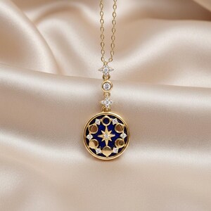 Puede incluir: Collar dorado con un colgante celestial. El colgante presenta un fondo de esmalte azul oscuro con un dise&ntilde;o de estrella y fases lunares, acentuado con cristales transparentes. El collar cuelga de una delicada cadena.