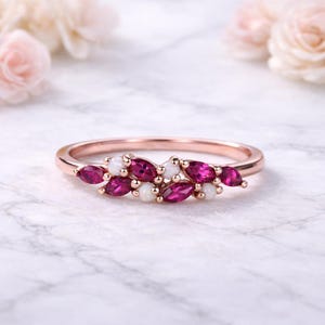 Könnte beinhalten: Roségoldener Ring mit einem Cluster aus marquiseförmigen, tiefrosa Edelsteinen und kleinen weißen Edelsteinen. Der Ring hat ein poliertes Roségoldband. Die Edelsteine sind in einem blattartigen Muster angeordnet.
