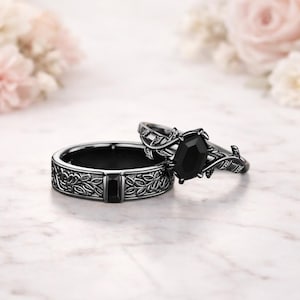 May include: Two matching black gemstone rings. One ring features a large, faceted black gemstone, while the other has a floral design with a rectangular black gemstone. The rings are set against a soft, blurred background.