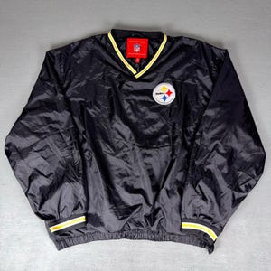May include: Black nylon pullover jacket with a V-neck and elastic cuffs. Features a yellow and white striped trim on the cuffs and collar. The Pittsburgh Steelers logo is on the chest.