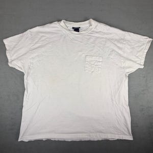 May include: A white, short-sleeved t-shirt with a chest pocket. The shirt has a crew neck and appears to be made of a soft, comfortable material. The shirt is plain and has a slightly wrinkled appearance.
