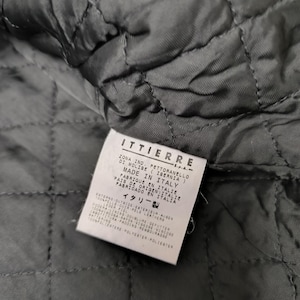 Puede incluir: Un interior de prenda acolchada negra con una etiqueta blanca rectangular de cuidado y origen. La etiqueta muestra el texto ITTIERRE S.p.A., Made in Italy, y enumera composiciones de materiales que incluyen 100% cuero exterior, 100% forro de viscosa y 100% relleno de poli&eacute;ster.