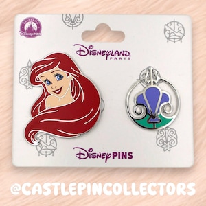 May include: Two Disney pins on a white card. One pin features Ariel with red hair and blue eyes. The other pin is a silver-colored design with purple and green accents. The card has the Disneyland Paris logo and Disney Pins text.