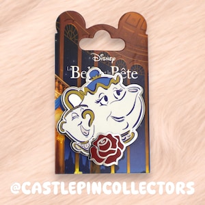 Può includere: Una spilla Disney in smalto con Mrs. Bric e Chicco de La Bella e la Bestia. La spilla è bianca con dettagli blu e oro e una rosa rossa. La spilla è su una carta con il titolo del film e il logo Disney.