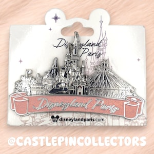 Puede incluir: Un pin plateado de Disneyland París con el castillo y Space Mountain, montado en una tarjeta blanca. El pin tiene una pancarta rosa con la inscripción "Disneyland París". La tarjeta tiene el logotipo y texto de Disneyland París.