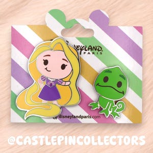 Pode incluir: Dois pins de esmalte num cartão de suporte às riscas com a marca Disneyland Paris. Um pin representa uma personagem de desenho animado com cabelo comprido amarelo e vestido roxo, o outro mostra um pequeno camaleão verde. Riscas diagonais.