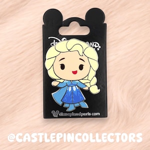 Könnte beinhalten: Ein Disney-Pin mit Elsa aus Frozen im Chibi-Stil. Der Pin befindet sich auf einer schwarzen Rückkarte mit Mickey Mouse-Ohren und dem Disneyland Paris-Logo. Der Pin ist hellblau, gelb und weiß.