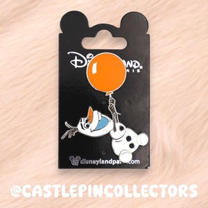 May include: A metal enamel pin featuring the character Olaf from Frozen holding a bright orange balloon. The pin is attached to a black backing card with the Disneyland Paris logo at the top and the website disneylandparis.com at the bottom.