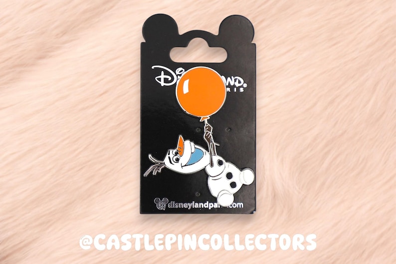 May include: A metal enamel pin featuring the character Olaf from Frozen holding a bright orange balloon. The pin is attached to a black backing card with the Disneyland Paris logo at the top and the website disneylandparis.com at the bottom.