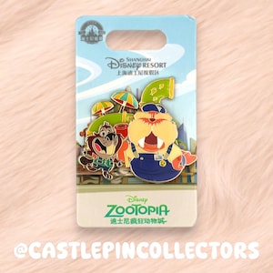 Könnte beinhalten: Ein Zootopia-Emaille-Pin vom Shanghai Disney Resort mit einem Walross in blauer Latzhose und einer kleineren braunen Figur vor einem Hintergrund aus bunten Regenschirmen und einem grünen Rohr, befestigt auf einer gebrandeten Pappkarte.