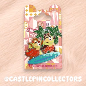 May include: Enamel pin showing Chip and Dale surfing on a blue surfboard, with palm trees and the text "it's a small world." The pin is on a pink and white patterned backing card with the Disneyland Paris logo.
